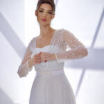 "Bella white two-piece gown with a fitted scuba inner dress and embroidered tulle cape adorned with pearls and glitter."